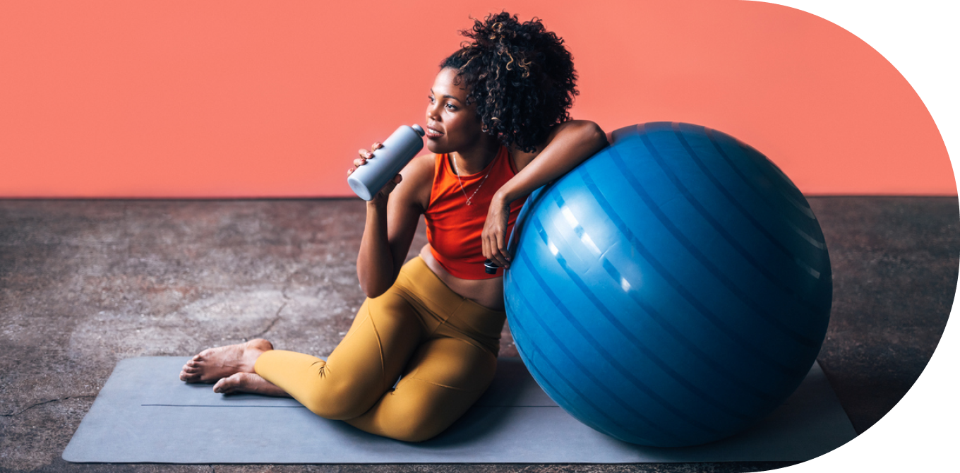 Mulher sentada encostada em bola azul tomando água